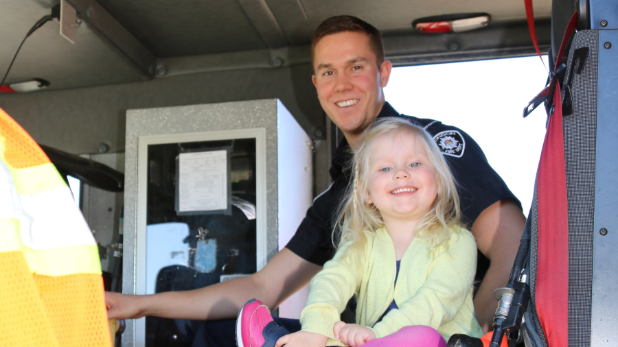 Photograph of Firefighter and Young Child in Fire Truck, smiling at the camera. 